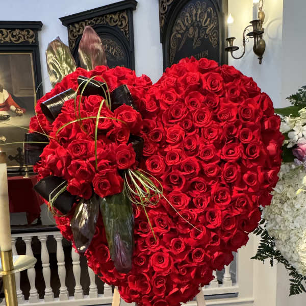 Heart-shaped red rose arrangement on an easel with black ribbon accents