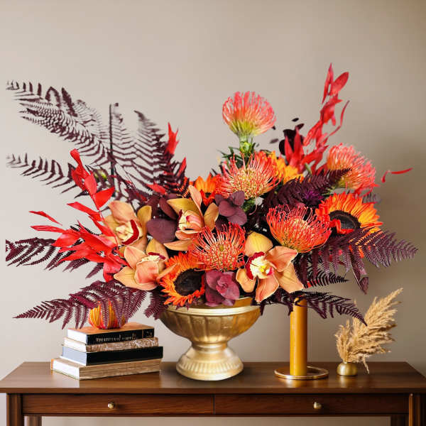Autumn floral arrangement in a gold vase with orange and burgundy blooms