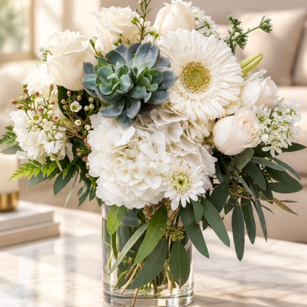 White floral bouquet with roses, gerbera daisies, hydrangea, and a succulent in a glass vase
