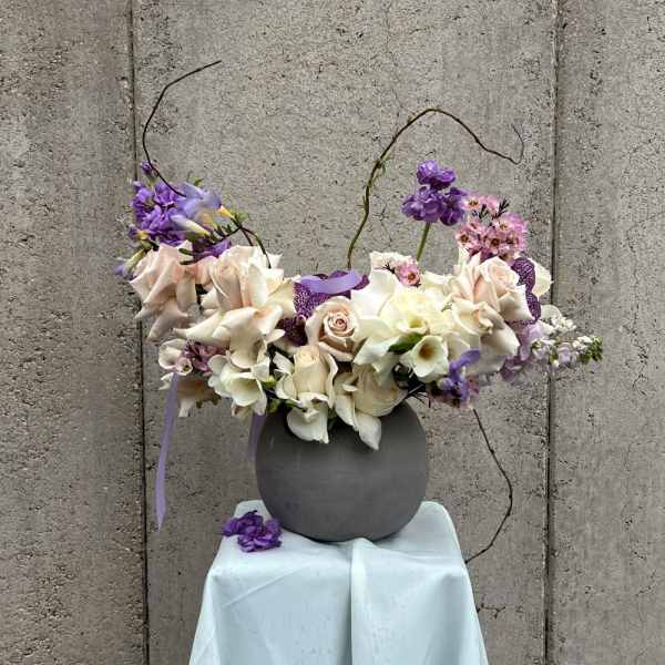 Purple and white floral arrangement in a gray vase on a draped pedestal