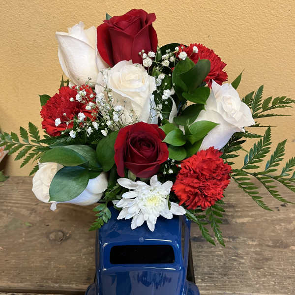 Red and white roses with red carnations in a blue truck vase