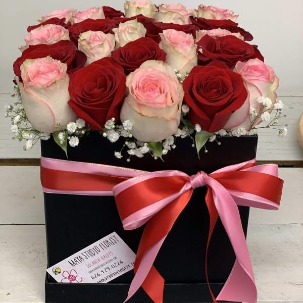 Red and blush roses arranged in a black box with a pink ribbon bow
