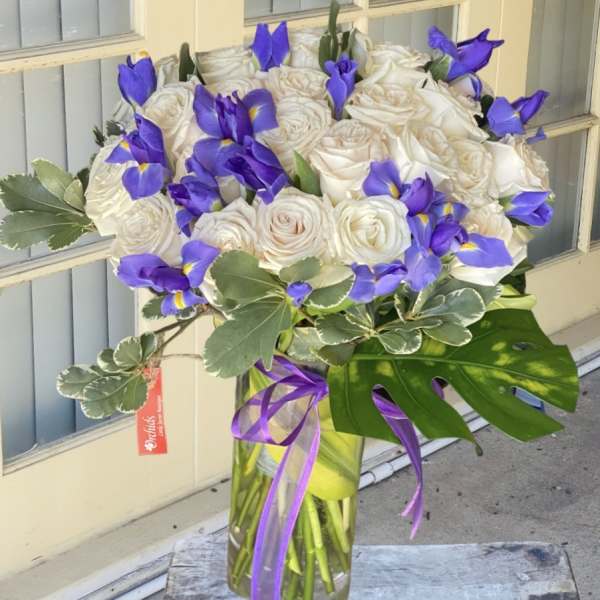 White roses and purple irises in a glass vase with a ribbon