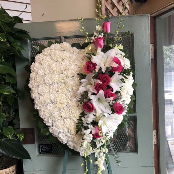 Heart-shaped white floral wreath with pink roses and lilies on an easel