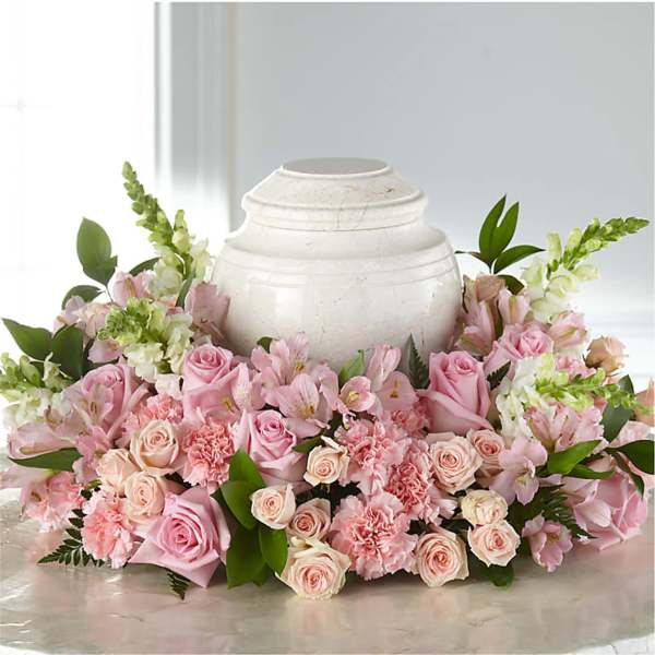 Pink roses and carnations arranged around a white urn