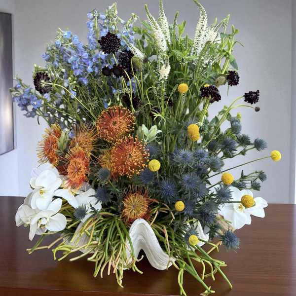 Mixed floral arrangement with blue, orange, white, and yellow blooms in a white vase