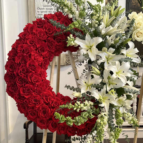 Large crescent floral wreath with red roses and white lilies on easels