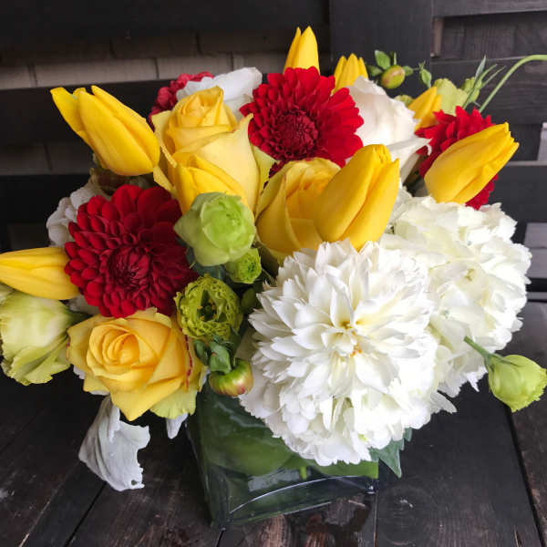 Bouquet of yellow tulips, red dahlias, white chrysanthemums, and yellow roses in a glass vase