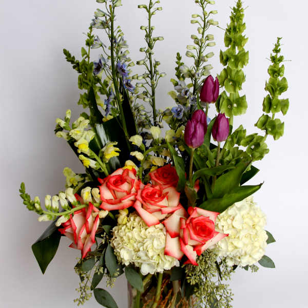 Tall mixed bouquet with roses, hydrangeas, and purple tulips in a glass vase