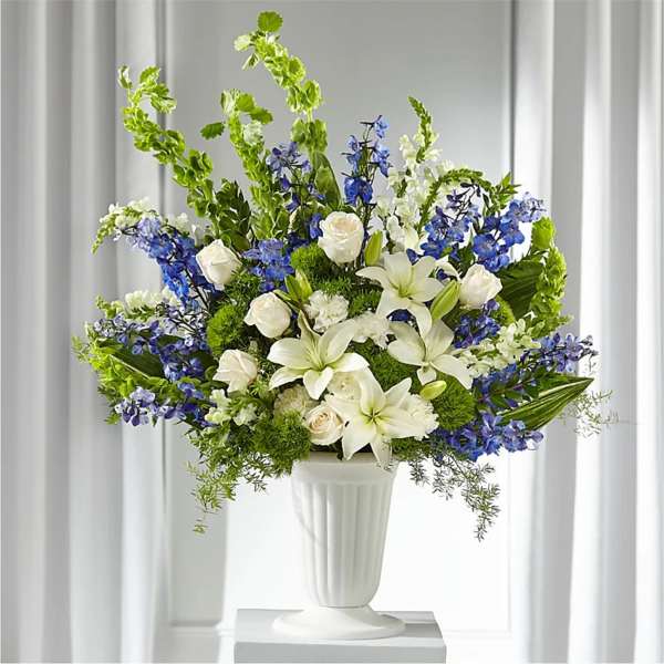 White lilies and roses arranged with blue flowers in a white vase