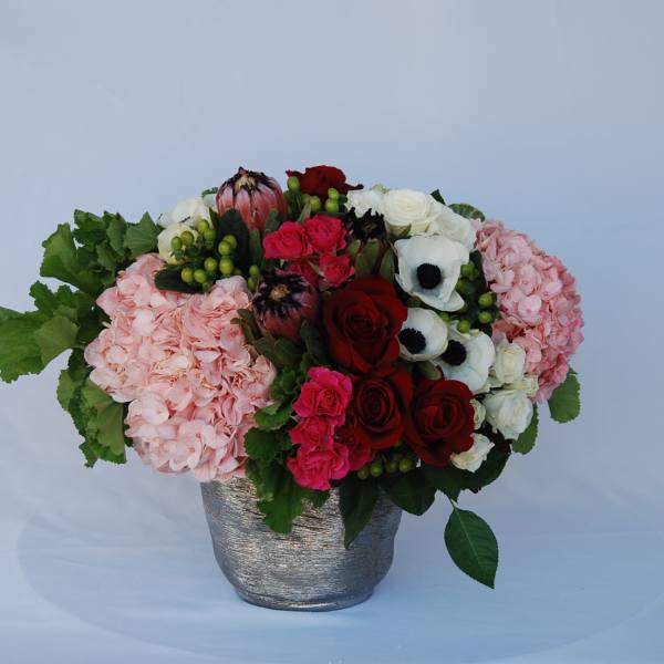 Mixed bouquet of roses, hydrangeas, and anemones in a silver vase