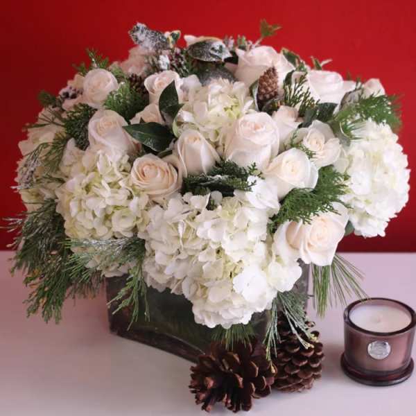 White roses and hydrangeas in a dark vase with pinecones and a candle