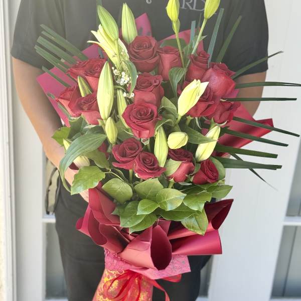 Bouquet of red roses and yellow lily buds wrapped in pink paper
