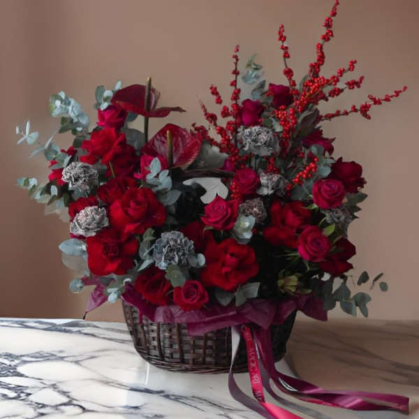Red roses and carnations in a wicker basket with eucalyptus and berry stems