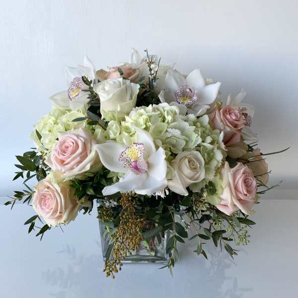 Bouquet of pale pink roses, white orchids, and green hydrangeas in a glass vase