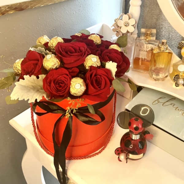 Red roses and gold-wrapped chocolates arranged in a round orange box