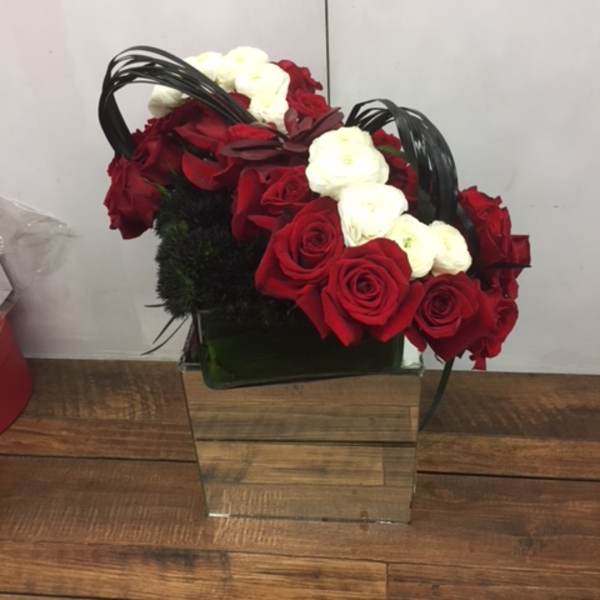 Red and white roses arranged in a square glass vase with black handles