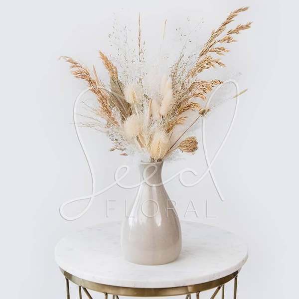 Dried grass arrangement in a beige vase on a round table