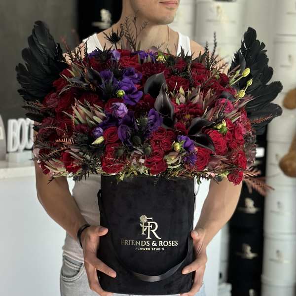 Large bouquet of red and purple flowers in a black box with black feathers.