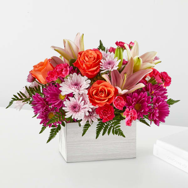 Bright mixed bouquet in a white square box with roses, lilies, and daisies
