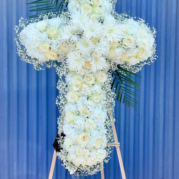 White floral cross arrangement on an easel with palm fronds