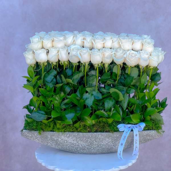 White roses arranged in a glittery silver vase with a blue ribbon
