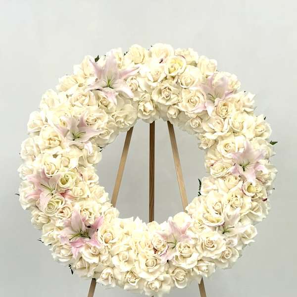Cream rose wreath with pale pink lilies on a wooden stand