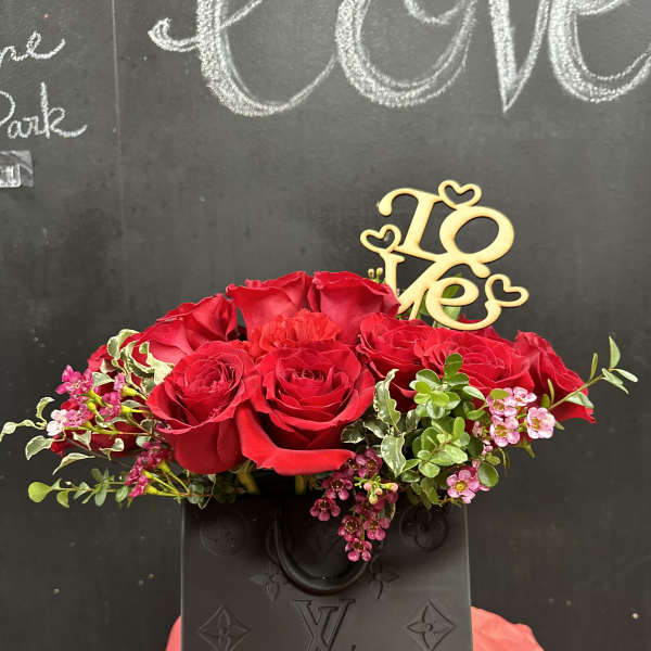 Red roses arranged in a black vase with a gold "Love" topper.