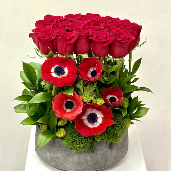Red roses and red anemones arranged in a gray vase