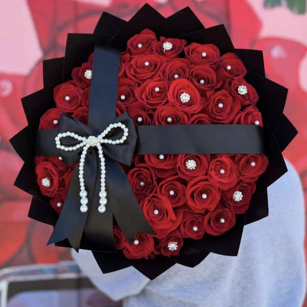 Bouquet of red roses wrapped in black paper with a pearl bow