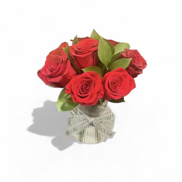 Red roses in a clear glass vase with a ribbon bow