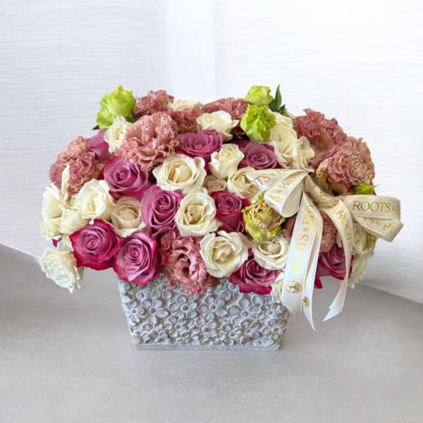 Pink and cream roses arranged in a textured square vase with a ribbon bow