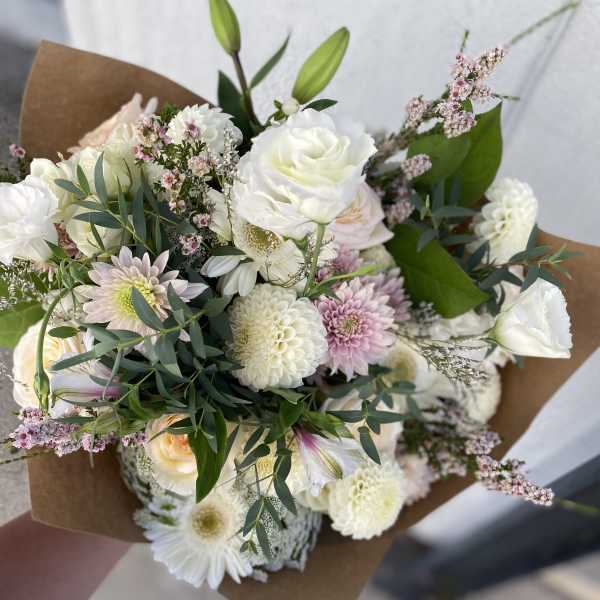 Hand-tied bouquet of white and blush flowers wrapped in brown paper