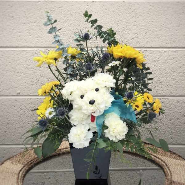 White flower arrangement shaped like a teddy bear with yellow blooms and a blue ribbon