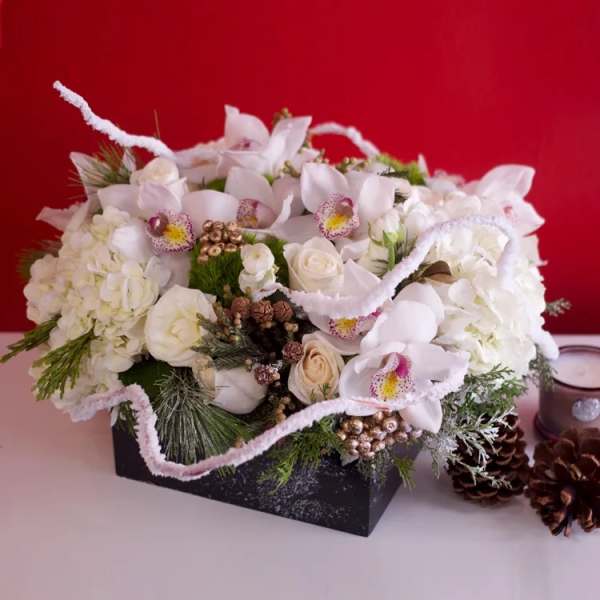 White floral arrangement in a black box with pinecones and ribbon