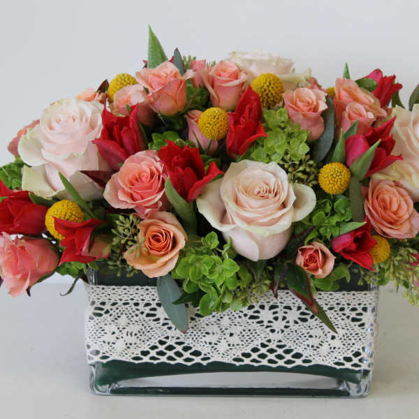 Mixed roses and yellow button flowers in a glass vase with lace trim