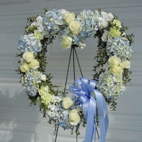 Heart-shaped floral wreath with pale blue and white flowers and a blue ribbon