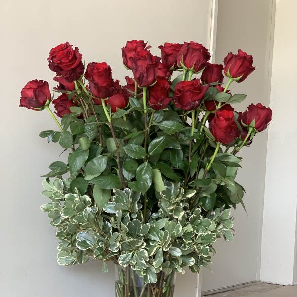 Tall vase arrangement of red roses with variegated greenery