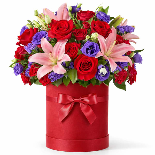 Red roses and pink lilies in a red hatbox with a ribbon