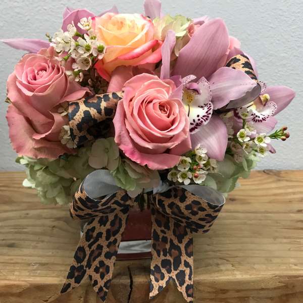 Pink roses and orchids arranged in a small vase with leopard-print ribbon.