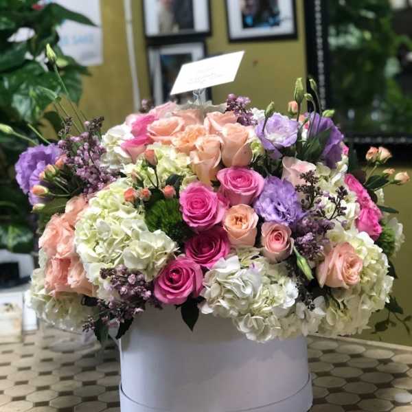 Round box arrangement of pink, peach, white, and lavender flowers