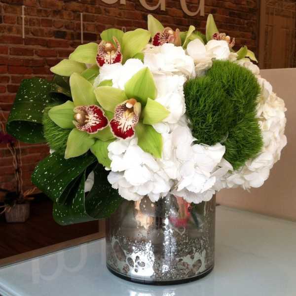 White hydrangeas and green orchids in a glass vase