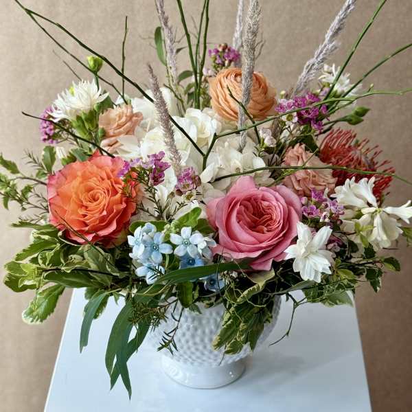 Mixed bouquet of roses, hydrangeas, and white blooms in a white vase