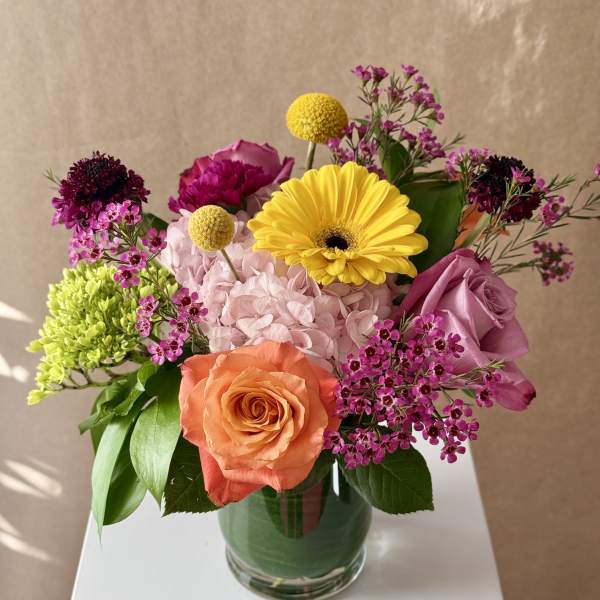Mixed bouquet in a glass vase with roses, hydrangea, and bright yellow blooms