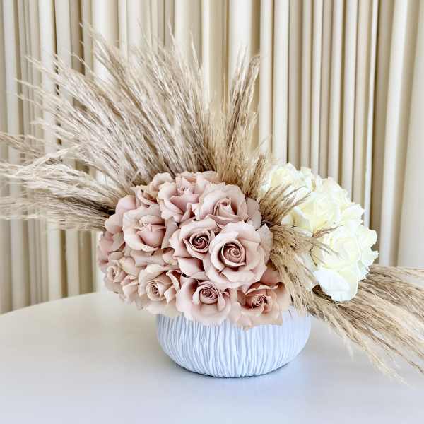 Asymmetrical arrangement of blush and ivory roses with pampas grass in a white bowl vase