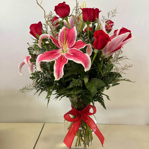 Red roses and pink lilies in a glass vase with a red ribbon