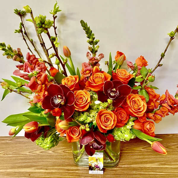 Orange roses and burgundy orchids in a clear glass vase