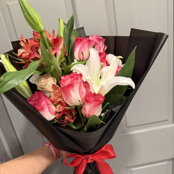 Bouquet of pink roses and white lilies wrapped in black paper with a red ribbon