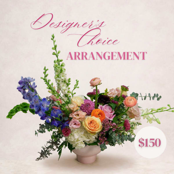 Mixed floral arrangement in a pale pink vase with blue, pink, orange, and white blooms