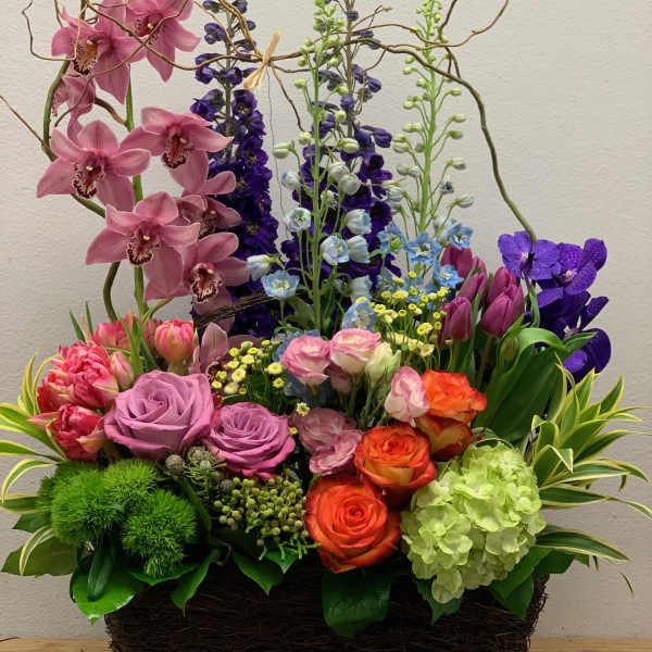Colorful mixed flower arrangement in a woven basket with tall orchid stems